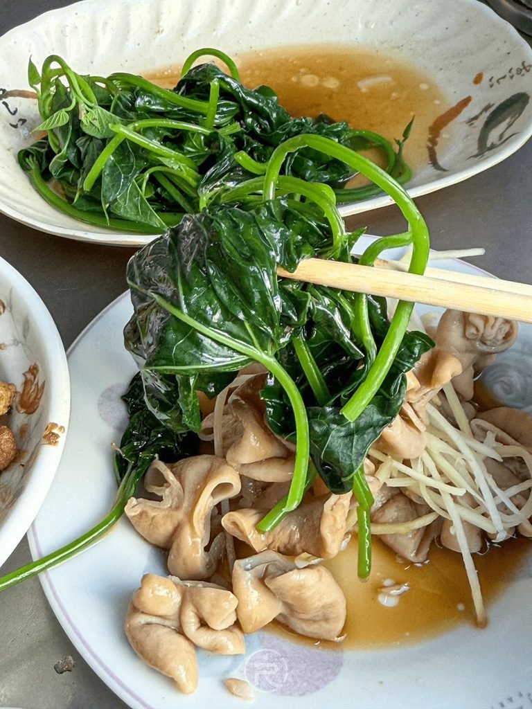 [夾起鮮綠燙地瓜葉]： 筷子夾起淋上豬油肉燥的新鮮燙地瓜葉，清脆爽口。