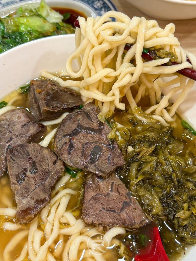 用筷子提起鼎吾記清燉牛肉麵的 Q 彈麵條,搭配厚實牛腱肉與酸菜。