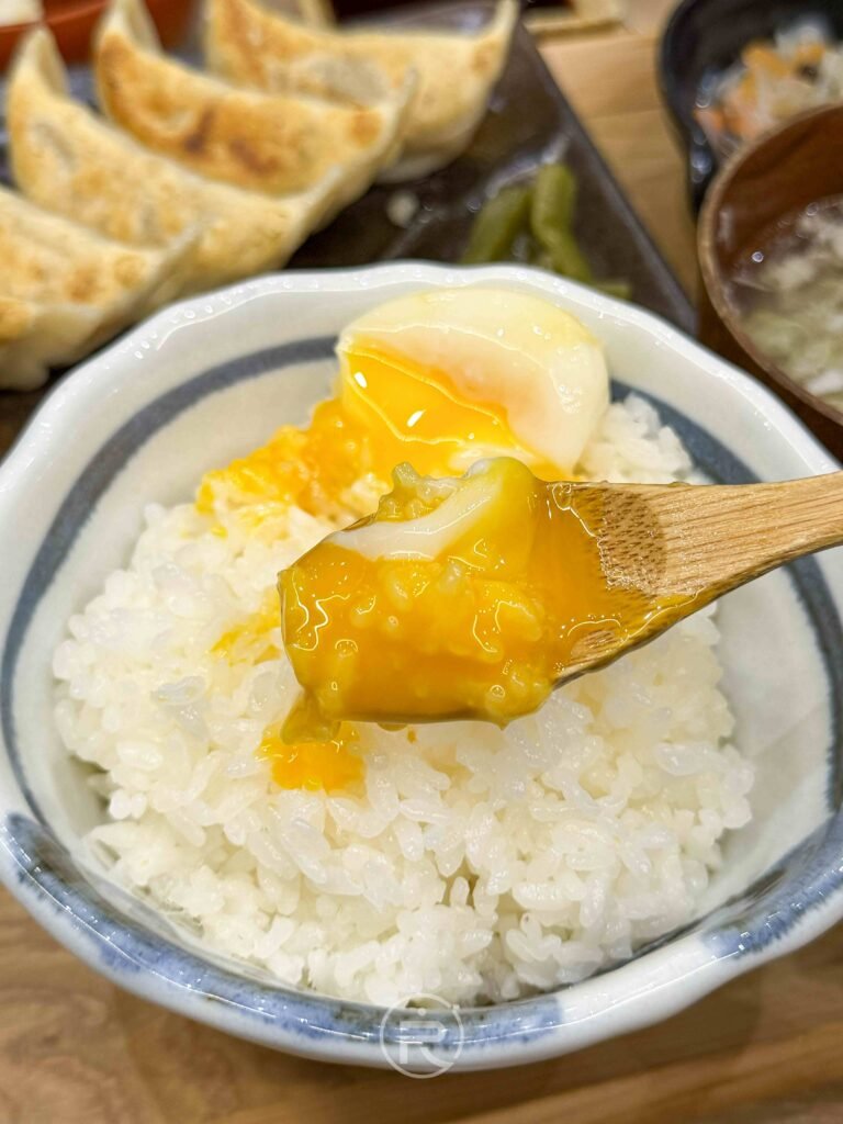 劃破溫泉蛋黃的療癒特寫，金黃色蛋液流淌在熱騰騰的白飯上。