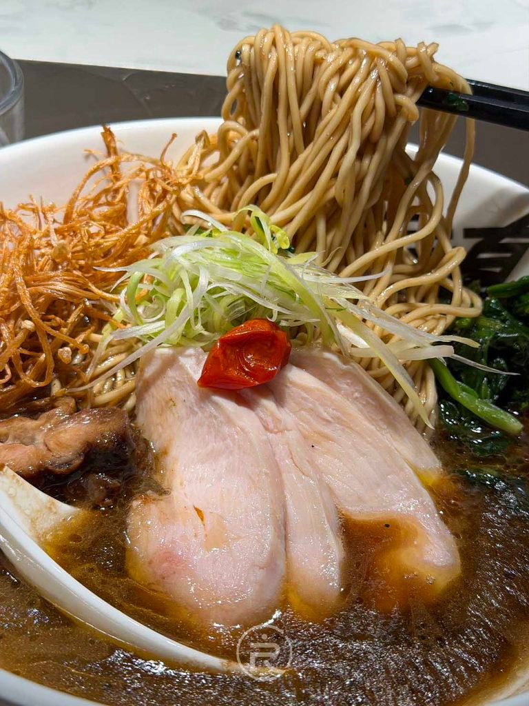 夾起庵仁真選用的「三森製麵」細麵，麵條吸附滿滿的熟成醬油雞豚白湯。