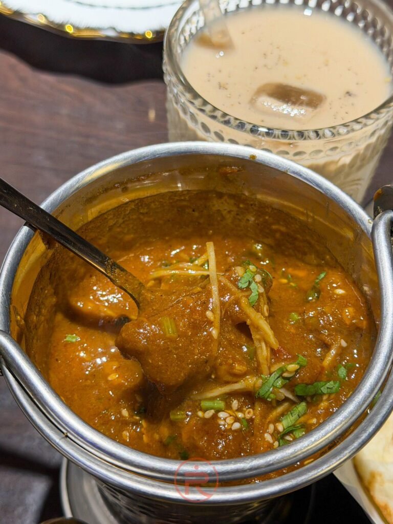 經典「香料羊肉咖哩 (Mutton Masala)」盛裝在傳統金屬鍋具中,鋪上薑絲提味。