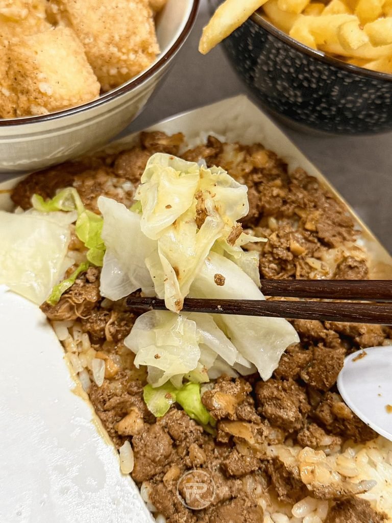 [夾起飯中青菜]： 筷子夾起肉燥飯盒內附帶的新鮮燙高麗菜，去油解膩。