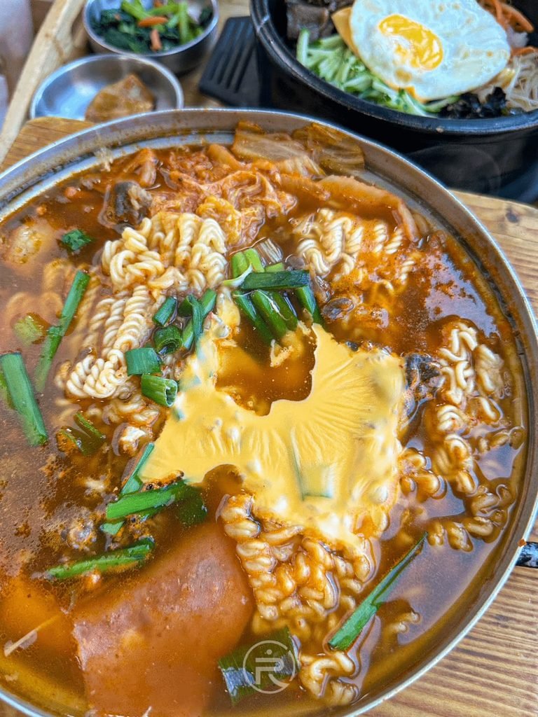 [起司融化鍋特寫]： 海鮮豬肉豆腐鍋特寫，融化的金黃切達起司覆蓋在 Q 彈韓式泡麵上。