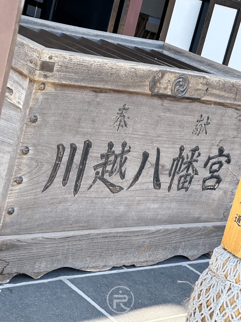 [賽錢箱銘刻]： 拜殿前刻有「奉獻 川越八幡宮」厚重質樸的木製賽錢箱。