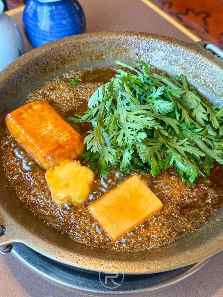 [翠綠茼蒿入鍋]： 放入新鮮日本茼蒿（春菊）與金黃生麩，增添蔬菜清新滋味。