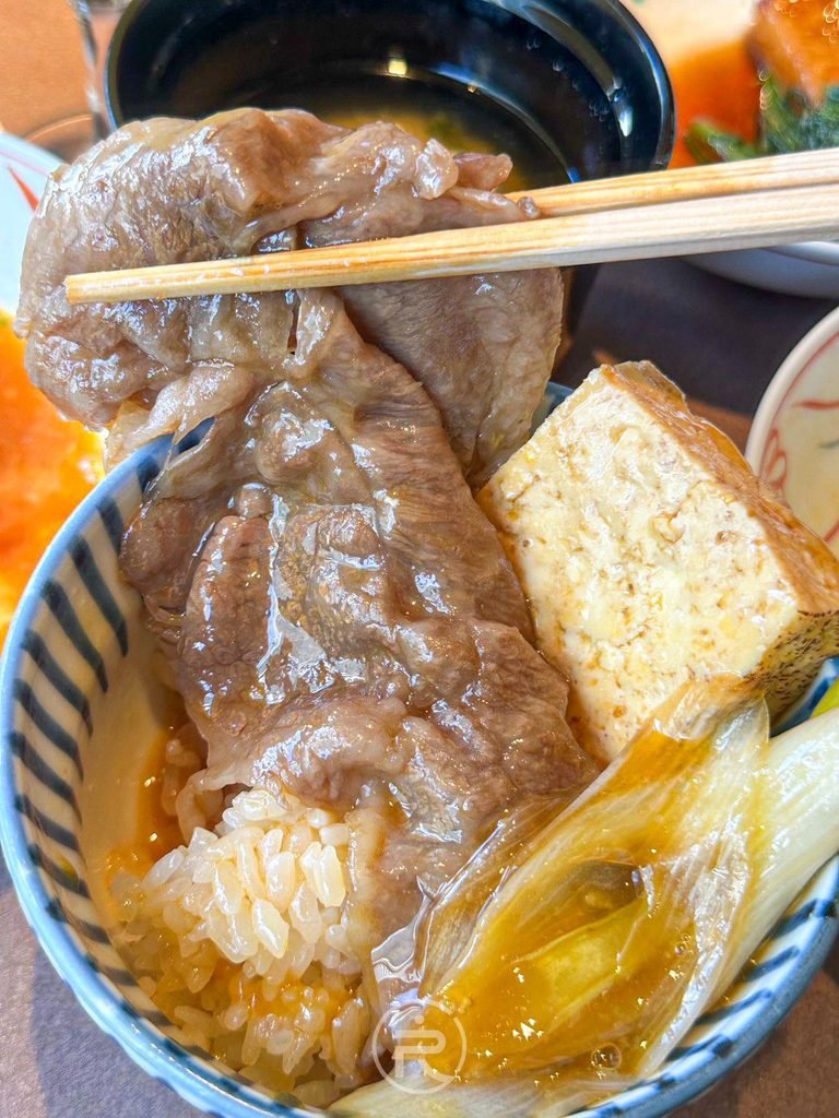  [夾肉配飯視角]： 筷子夾起大片和牛肉蓋在白飯與烤豆腐上，令人食指大動。
