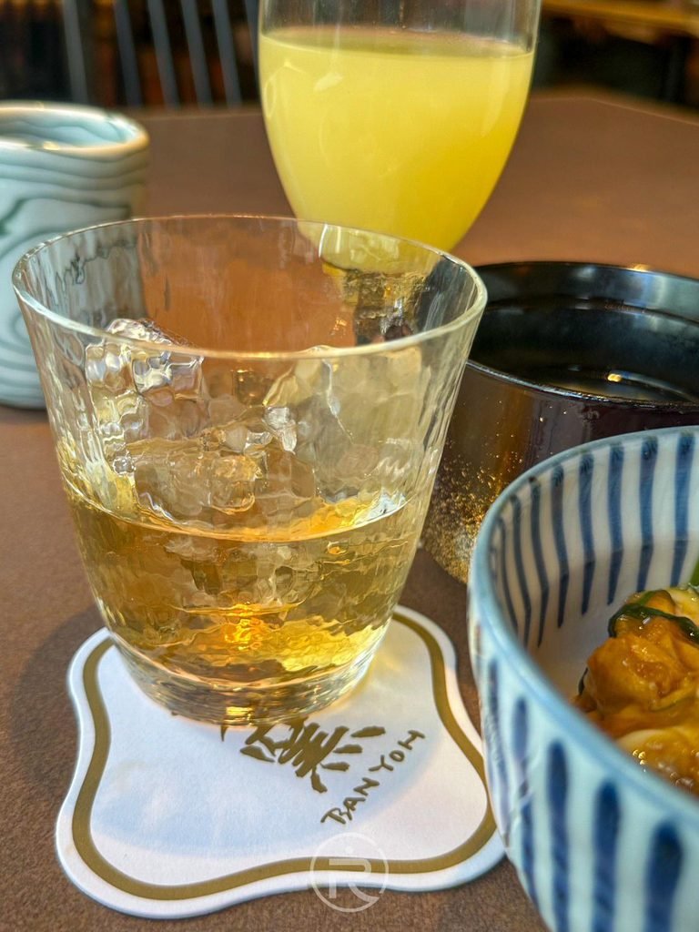 [佐餐酒水特寫]： 放置於今半萬窯標誌吸水紙杯墊上的清涼威士忌蘇打調飲。