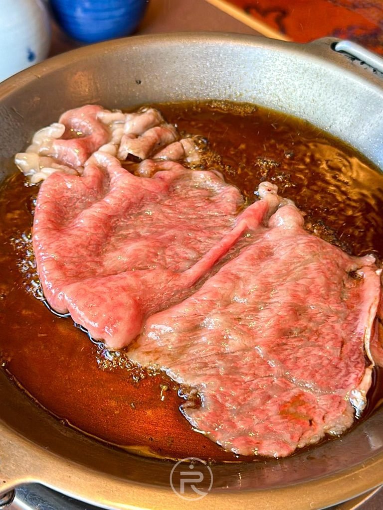 [涮煎和牛肉片]： 女將親自桌邊服務，將大片黑毛和牛放入滾燙壽喜燒醬汁中精準熟成。
