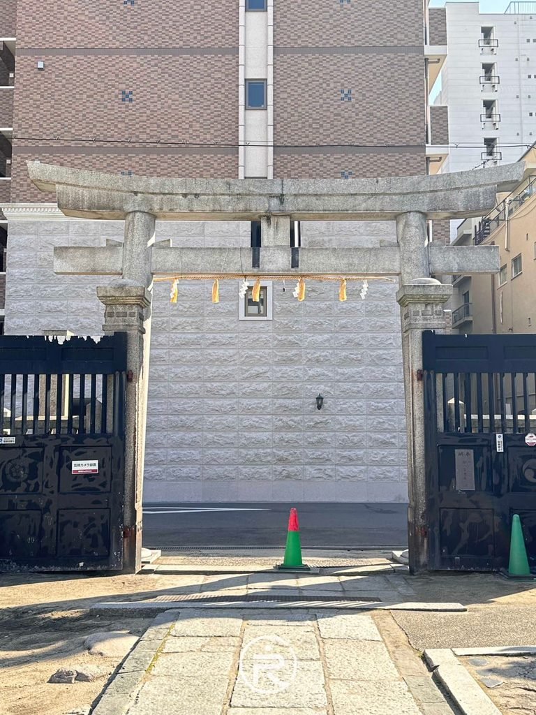 [石造鳥居與大門]： 從境內向外遠眺石造鳥居與現代公寓街景，展現古今交融感。
