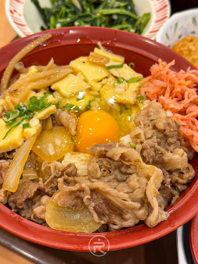 碗中鋪滿玉子燒塊、洋蔥牛肉、紅薑與中央鮮豔金黃生蛋黃特寫。