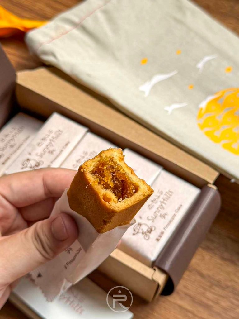  [手持斷面與禮盒]： 手拿咬開的鳳梨酥與中秋禮盒背景合照，金黃色澤極具食慾感。