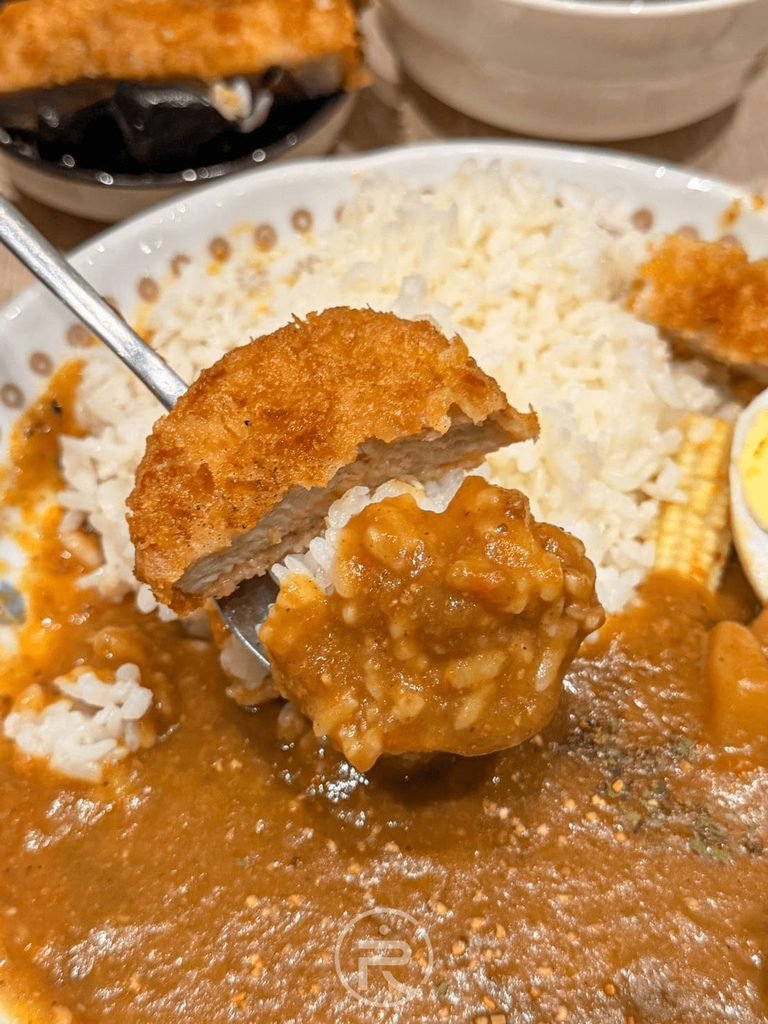  [舀起豬排咖哩飯]： 湯匙舀起吸附濃郁熟成咖哩醬的白飯與酥脆黃金炸豬排切片。