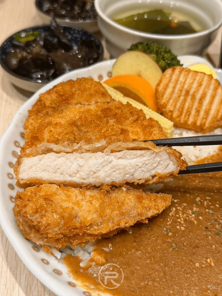 [筷夾厚切豬排斷面]： 筷子夾起厚切豬排展示扎實肉質厚度，肉質粉嫩且帶有肉汁。