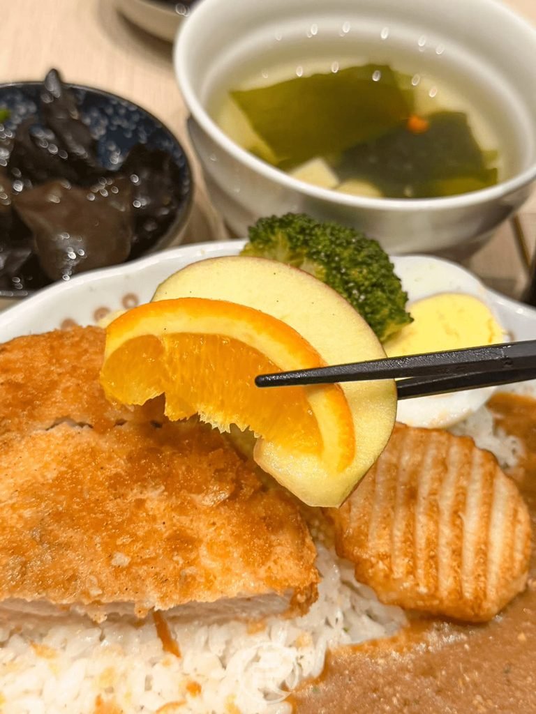  [舀起新鮮柳橙]： 湯匙舀起盤中的新鮮切片柳橙，巧妙利用果酸平衡咖哩濃郁感。