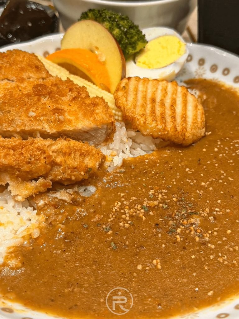 [熟成咖哩醬與白飯]： 浸潤在深色熟成咖哩醬中的米飯，灑滿白芝麻增添香氣。