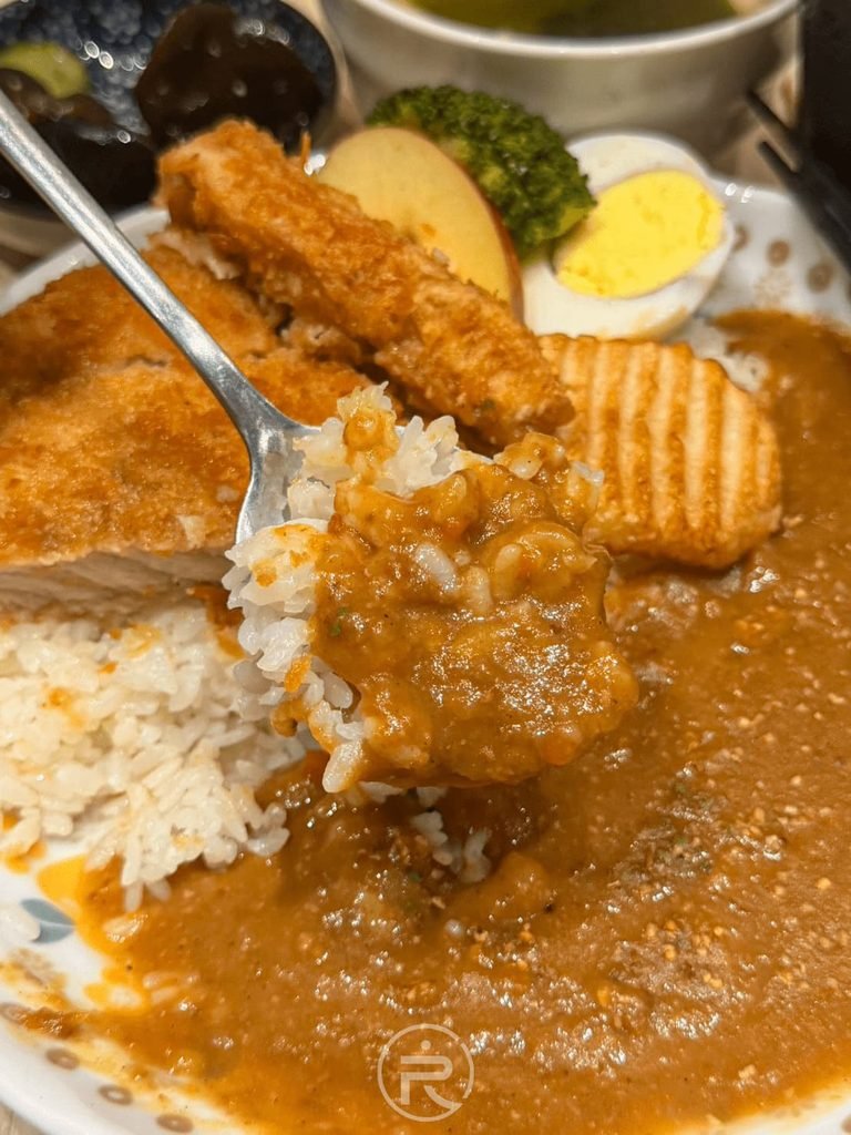 [大口吃豬排咖哩]： 湯匙舀起沾滿濃郁咖哩醬的白飯搭配一塊酥脆炸豬排。