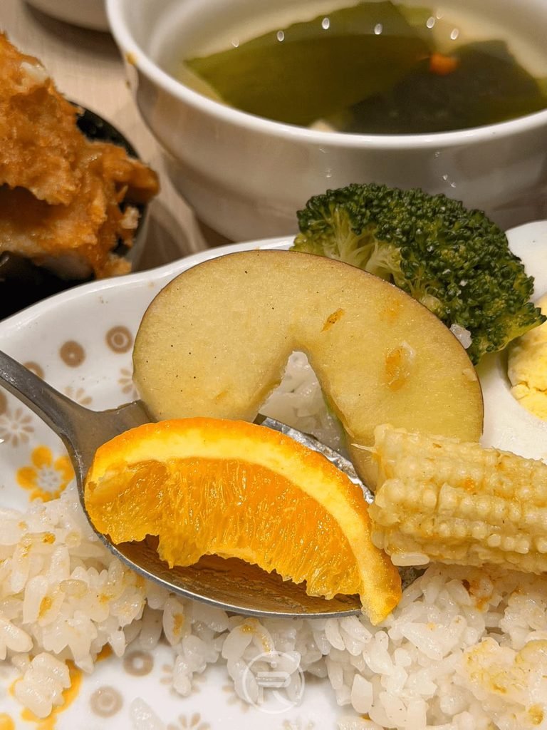  [舀起蘋果與玉米筍]： 湯匙舀起鮮甜的蘋果切片與玉米筍配菜。