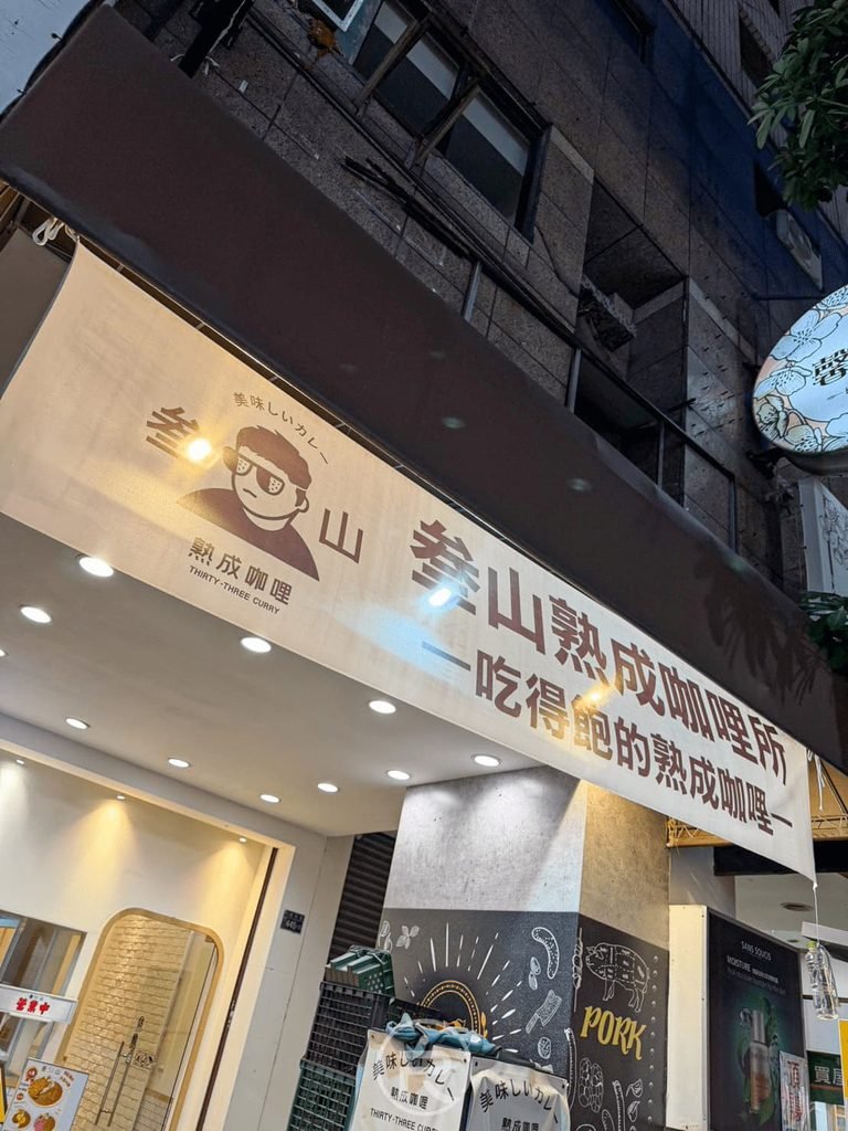  [店面外觀與標語]： 叁山熟成咖喱所店面夜景，上方標語寫著「一吃成癮的熟成咖哩」。