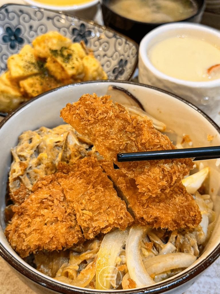 [夾起厚切肉排]： 筷子夾起厚實且無油耗味的厚切豬排，金黃麵衣非常誘人。