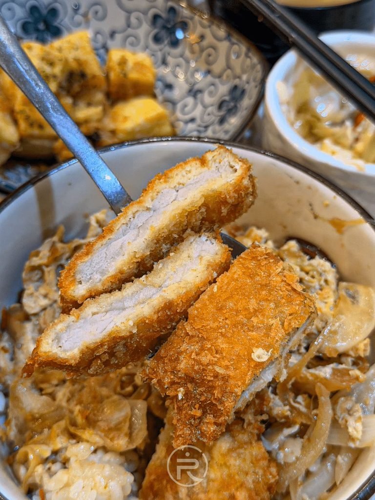  [豬排蓋飯近拍]： 勝利豬排蓋飯特寫，金黃麵衣豬排切片鋪在滑嫩洋蔥洋蛋上。