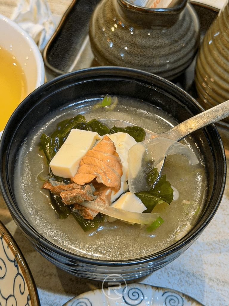  [舀起鮮魚味噌湯]： 鮮魚味噌湯料多實在，湯匙舀起大塊魚肉與燉煮入味的嫩豆腐。