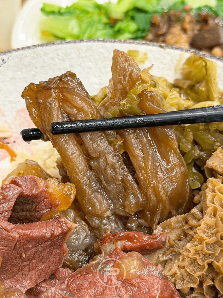 [夾起大塊牛筋]： 筷子夾起透亮厚實的紅燒牛筋，膠質豐富且口感極佳。