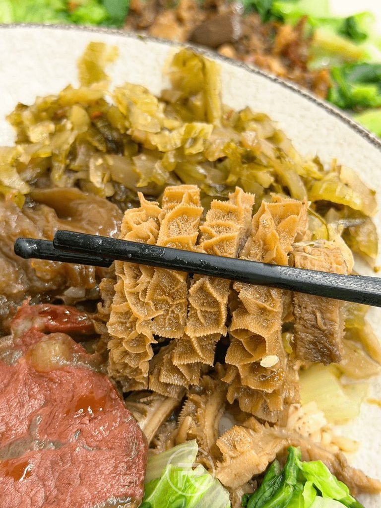 [夾起蜂巢牛肚]： 筷子夾起滷得入味金黃的蜂巢牛肚，紋理分明彈牙脆口。