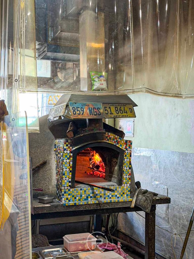 [窯烤工作區全景]： 窯烤爐工作台與牆上裝飾的美式復古車牌造景。