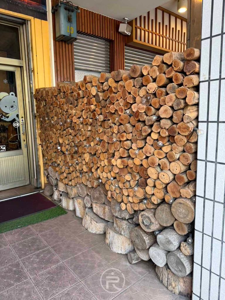 [店外木柴堆牆]： 店門口整面由圓木整齊堆砌而成的木柴牆，天然柴香撲鼻。