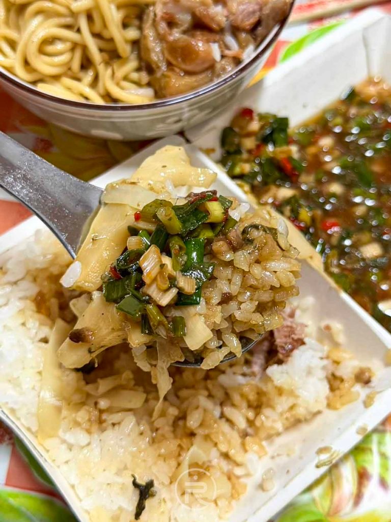  [蔥辣醬拌飯]： 湯匙舀起淋滿康康豬靈魂自製蔥辣醬的滷肉飯，蔥香誘人。