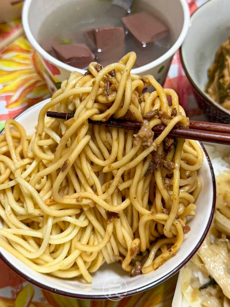 [大口夾起炒麵]： 用筷子拌勻提起金黃油亮的肉燥炒麵，香味四溢。