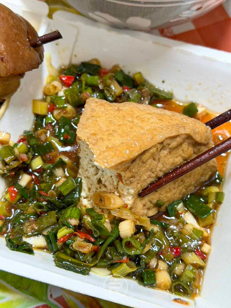 [油豆腐沾醬]： 咬開的油豆腐內部白嫩，沾裹微辣鹹香的蔥花醬汁。