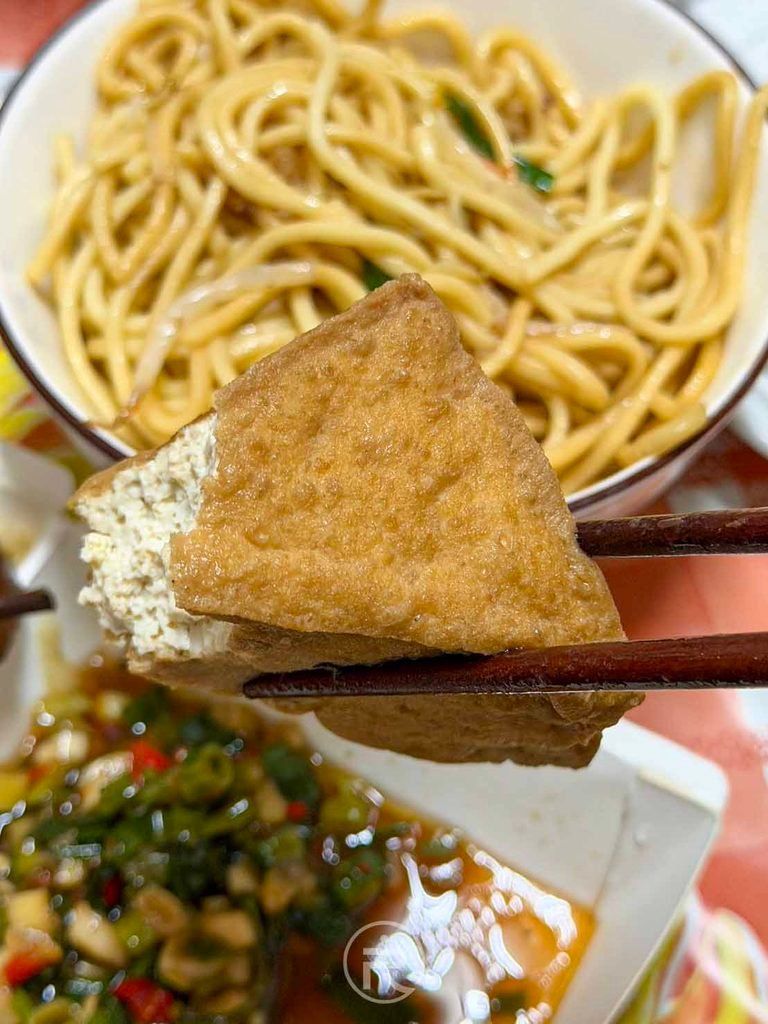  [夾起油豆腐]： 筷子夾起吸滿湯汁精華的三角油豆腐，鮮嫩可口。