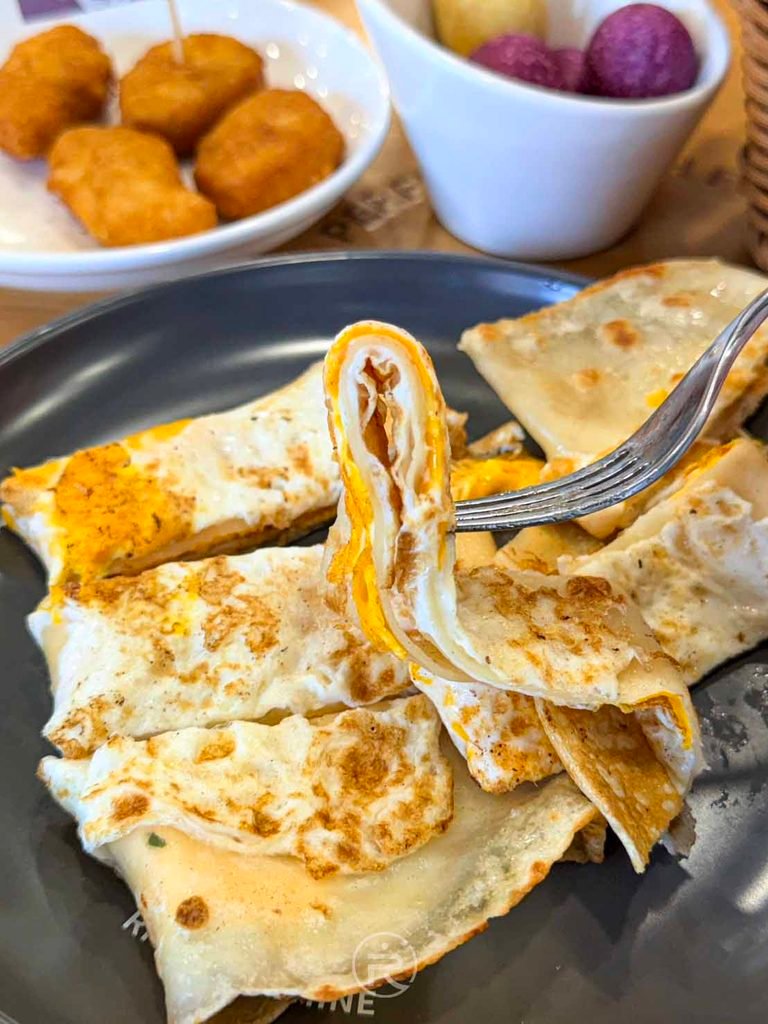 [叉起蛋餅瞬間]： 叉子夾起熱騰騰的雙蛋蛋餅，蛋液與餅皮緊密結合。