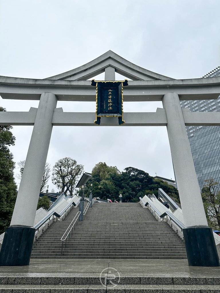 [石造巨大山王鳥居]： 永田町側寬廣參道上的巨大白色石造山王鳥居與氣派的男坂石階。