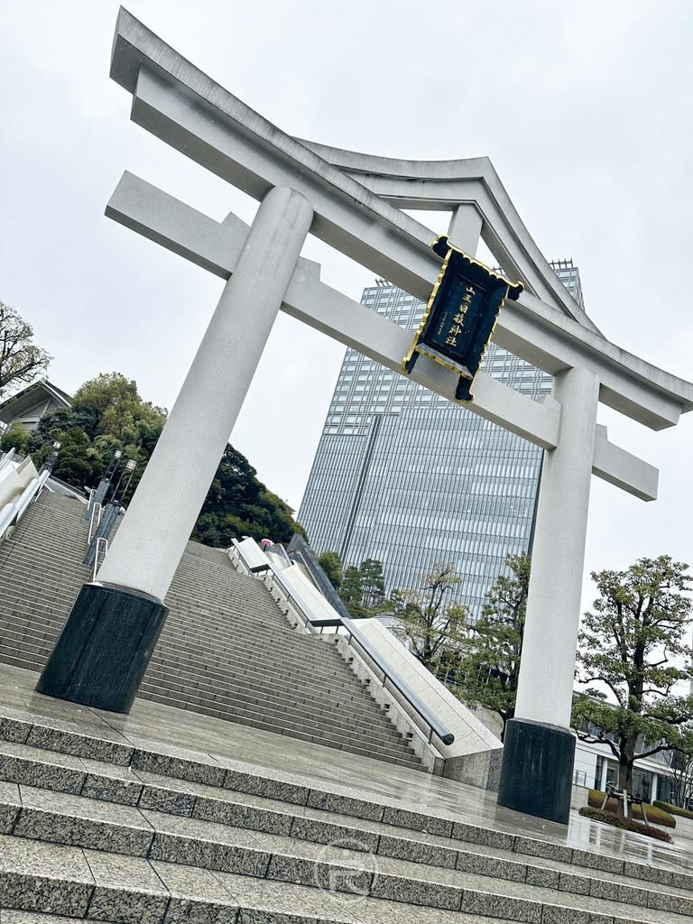 [摩天樓與鳥居同框]： 仰望宏偉的石造大鳥居，後方現代摩天大樓聳立，展現古今強烈對比。