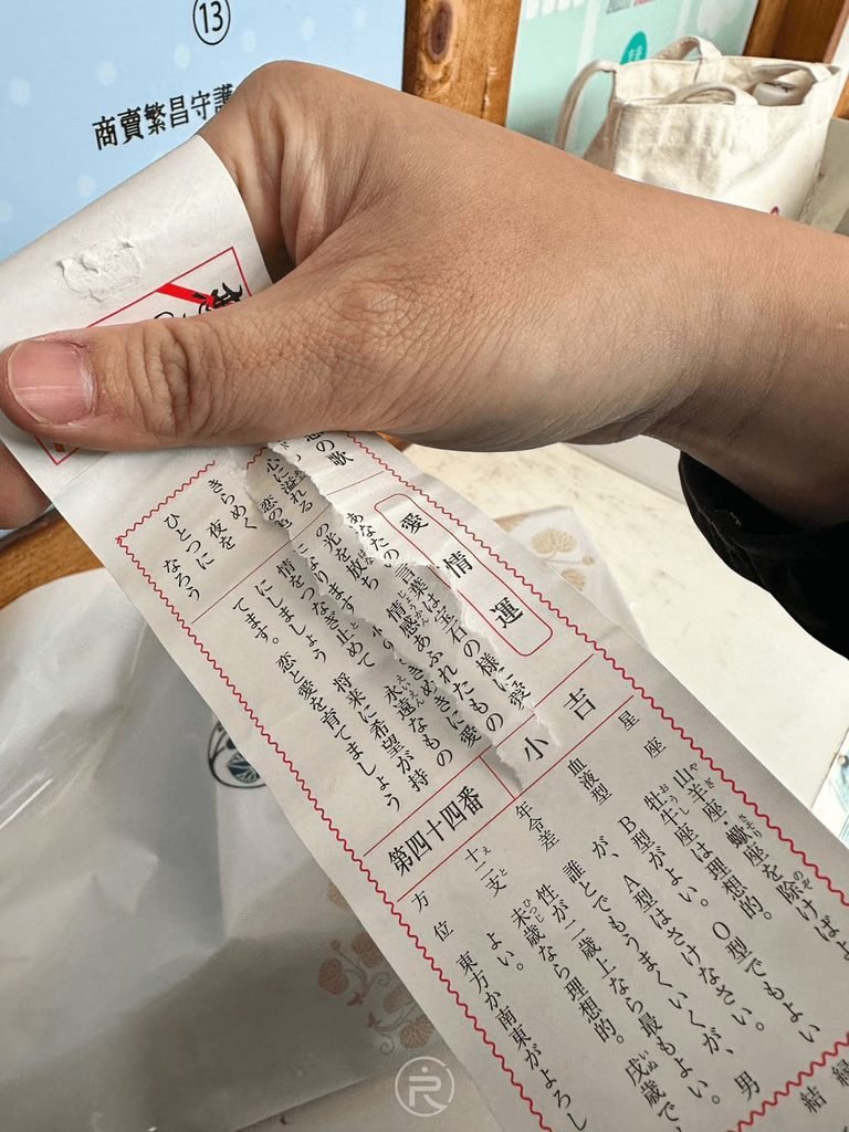  [展開小吉籤詩]： 手持在日枝神社抽到的日文御神籤（おみくじ）紙本，細讀神明指引。
