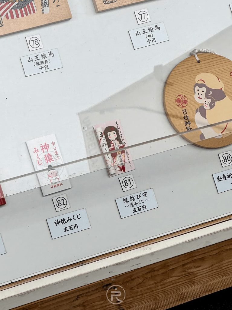  [神猿御守展示櫃]： 櫥窗展示的日枝神社特色神猿御守、緣結吊飾與木製御守。