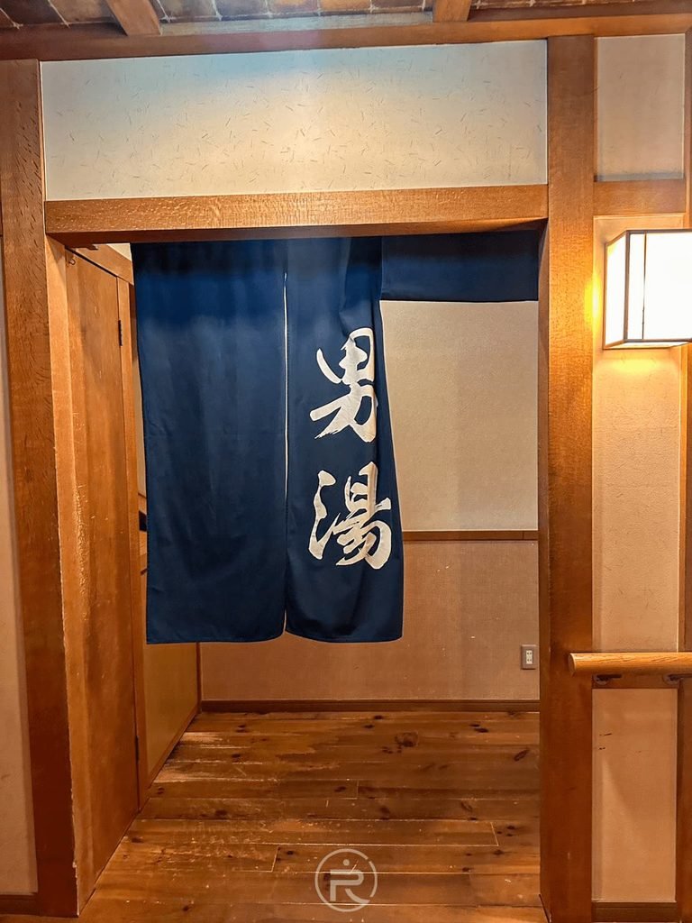  [男湯藍色暖簾入口]： 春日部溫泉「男湯」入口木造拱門與深藍色日式門簾。
