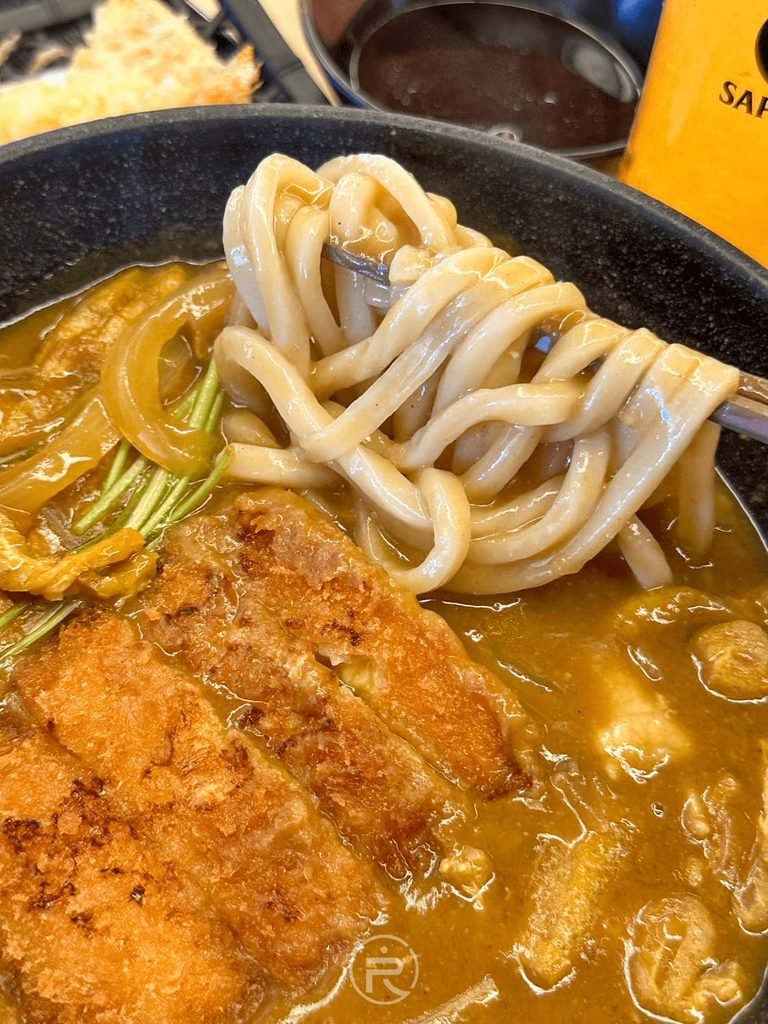 [夾起咖哩烏龍麵]： 筷子夾起吸飽濃厚咖哩醬汁的 Q 彈粗烏龍麵條，香氣撲鼻。
