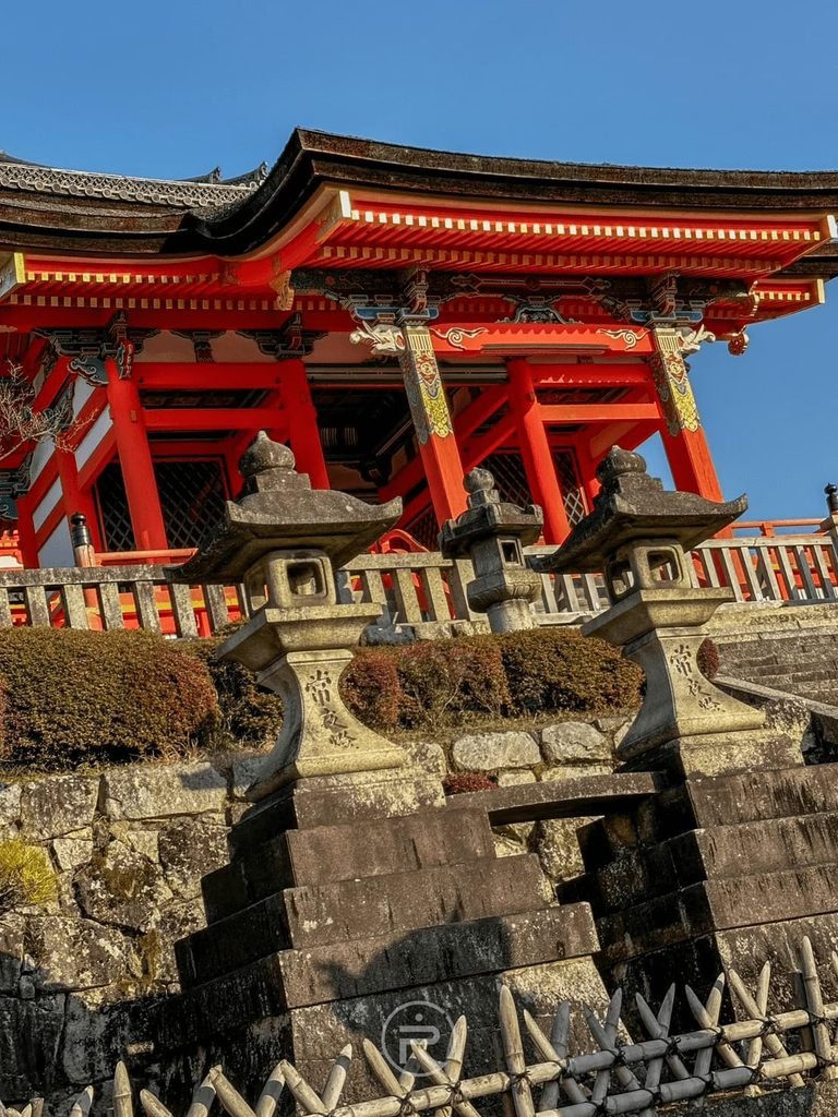 [石燈籠與朱紅山門]： 古樸石燈籠與石階後方巍峨矗立的朱紅色山門建築。