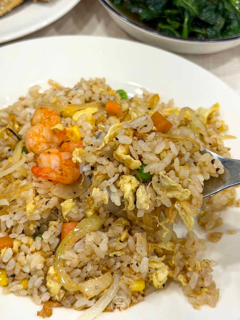  [湯匙舀起炒飯]： 湯匙舀起粒粒分明、融入洋蔥與碎蛋香氣的蝦仁蛋炒飯。