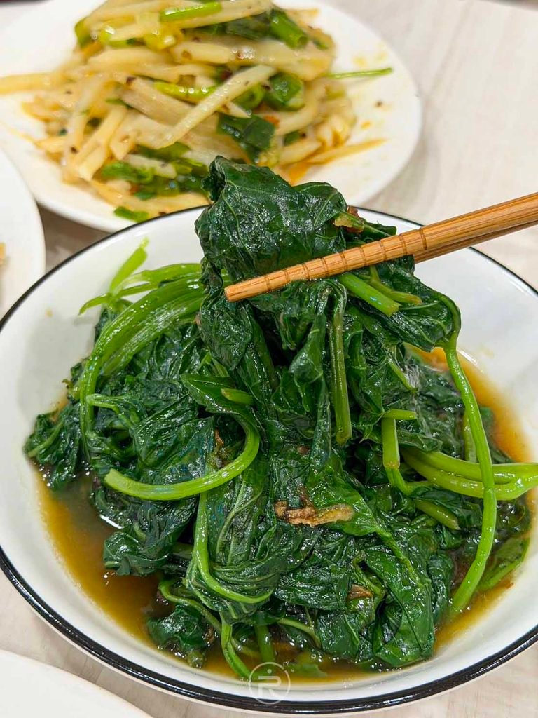  [筷夾燙青菜]： 筷子夾起鮮綠脆嫩的燙地瓜葉，口感細緻去油解膩。