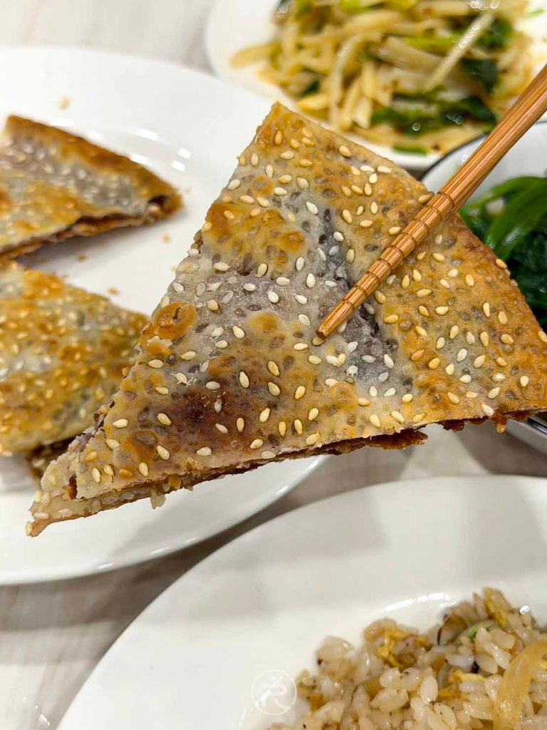 [筷夾紅豆鍋餅]： 筷子夾起三角形紅豆沙鍋餅，外皮微焦金黃酥脆。