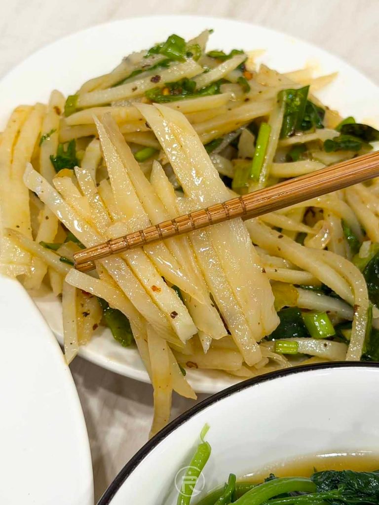 [夾起麻辣脆薯絲]： 筷子夾起爽脆微透的馬鈴薯絲，麻辣香濃極度開胃下飯。