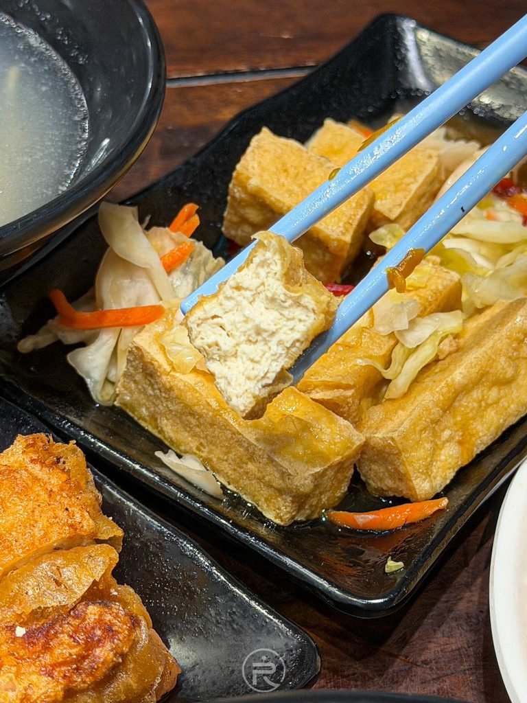  [筷夾臭豆腐斷面]： 筷子夾起外酥內嫩的臭豆腐塊，內部氣孔吸滿醬汁。
