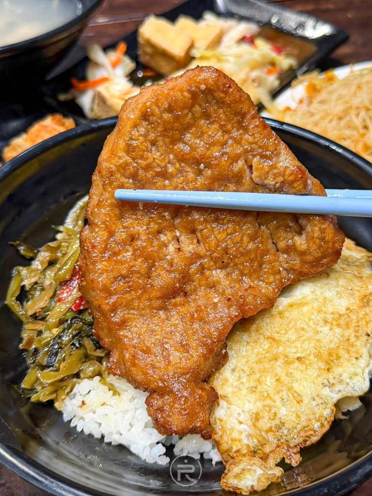 [整塊燒肉排特寫]： 筷子夾起整塊大份量現炸燒肉排，醬色透亮誘人食慾。