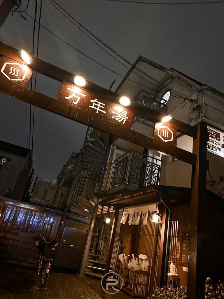 [夜間巷弄木門拱門]： 新宿巷弄內的百年錢湯「萬年湯」夜間入口，發光招牌指引旅人進入。
