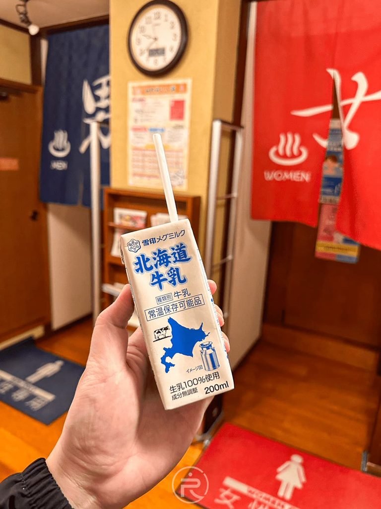  [手持北海道牛乳]： 泡完湯後的靈魂儀式：手持冰涼「北海道牛乳」在男湯女湯門簾前合影