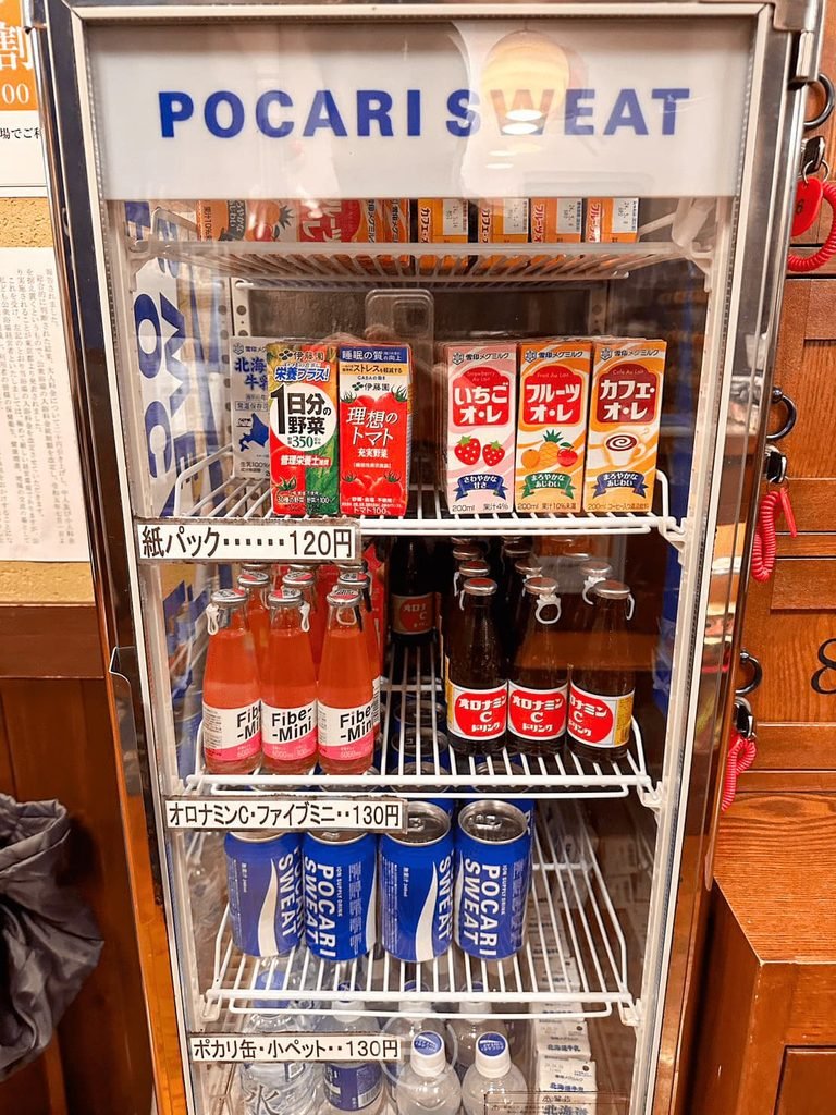  [冷藏飲料販賣機]： 玻璃冷藏櫃內擺滿冰鎮寶礦力水得、咖啡牛奶、茶飲與各式汽水。
